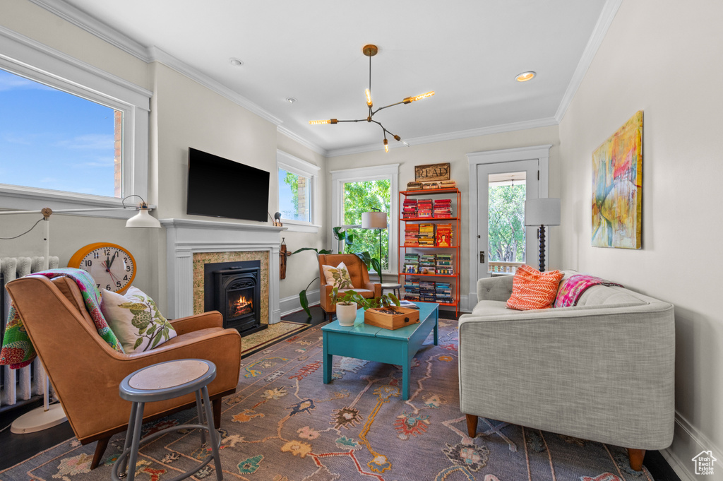 Living room featuring a chandelier, crown molding, a warm lit fireplace, and wood finished floors