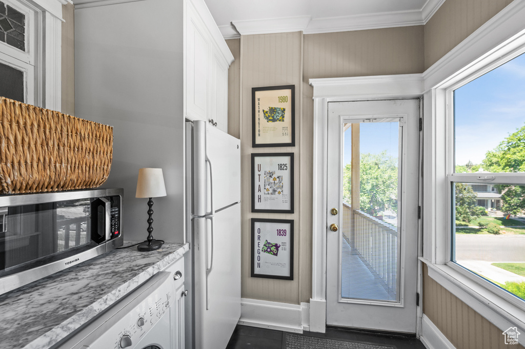 Kitchen with freestanding refrigerator, ornamental molding, washer / dryer, white cabinetry, and stainless steel microwave