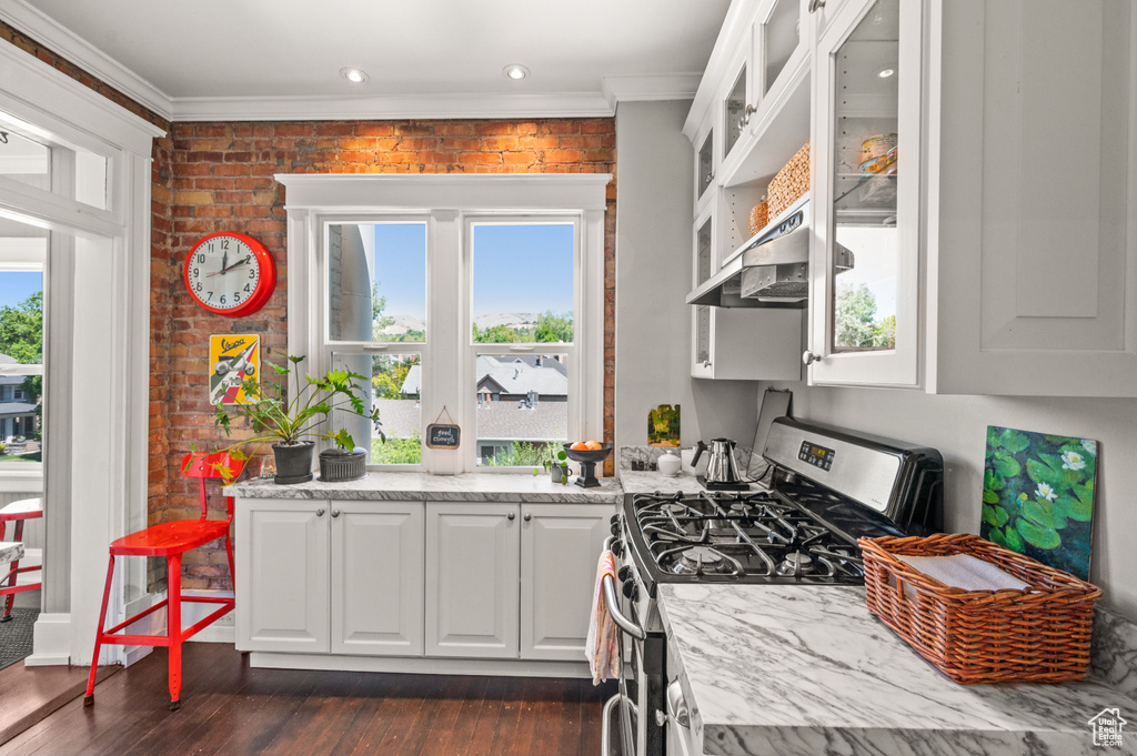 Kitchen with stainless steel range with gas cooktop, brick wall, ornamental molding, white cabinetry, and ventilation hood