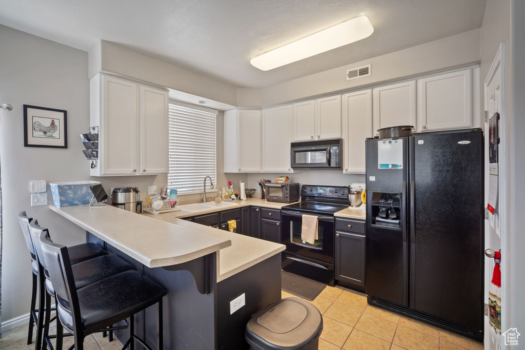 Kitchen featuring black appliances, a peninsula, white cabinets, and a kitchen bar