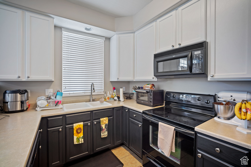 Kitchen with black appliances, white cabinetry, light countertops, light tile patterned floors, and dark cabinets