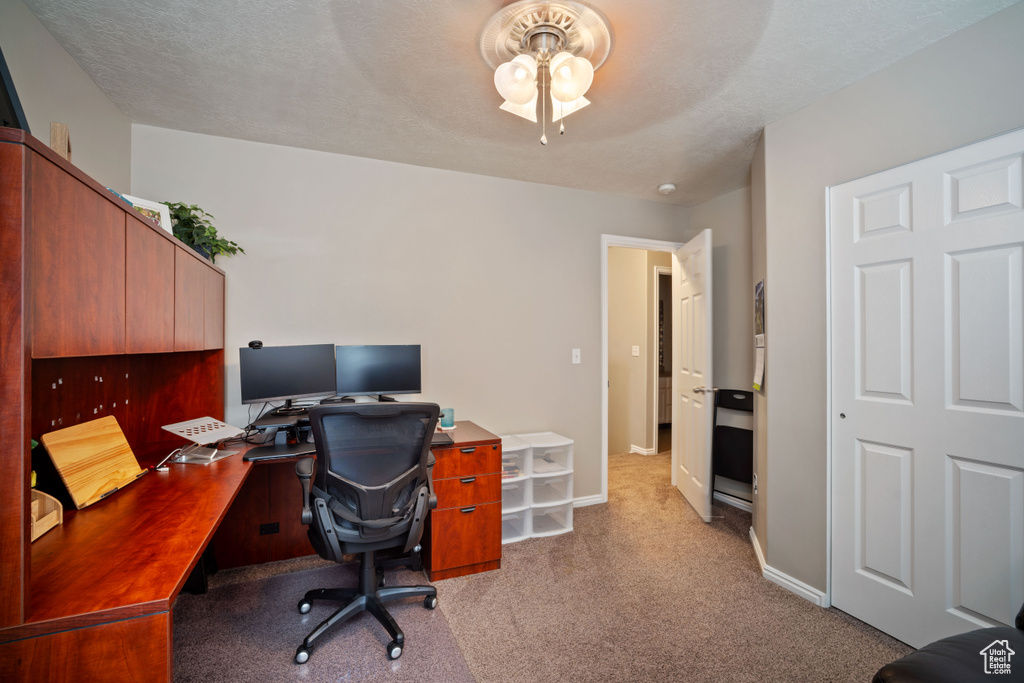 Carpeted home office featuring a ceiling fan and baseboards