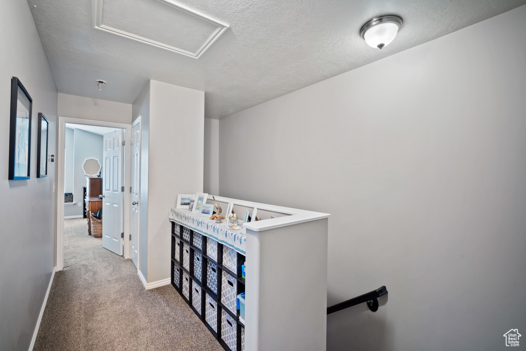 Hallway featuring an upstairs landing, attic access, carpet floors, and a textured ceiling