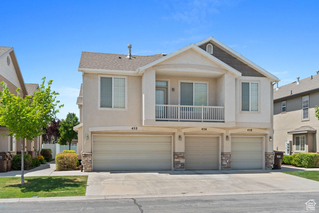 Multi unit property featuring an attached garage, stone siding, concrete driveway, and stucco siding