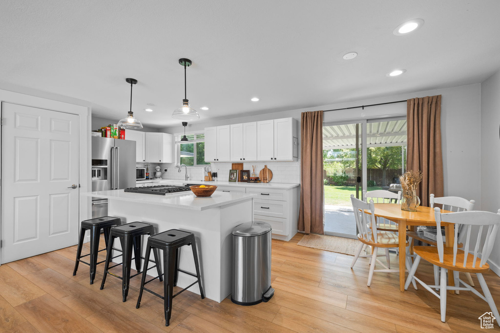 Kitchen with stainless steel appliances, light wood-type flooring, a kitchen bar, recessed lighting, and white cabinetry