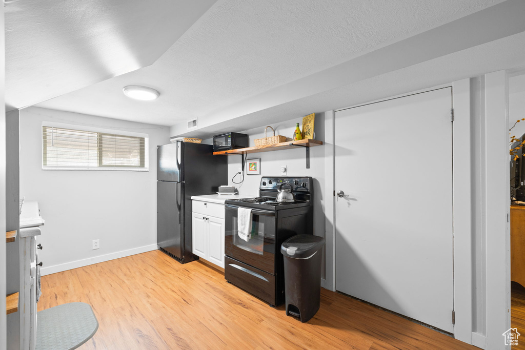 Kitchen with black appliances, light wood-type flooring, open shelves, light countertops, and a textured ceiling