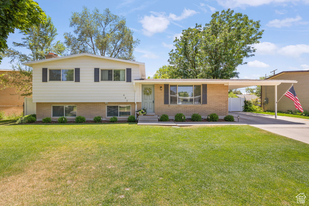 Tri-level home with brick siding, concrete driveway, an attached carport, and a chimney