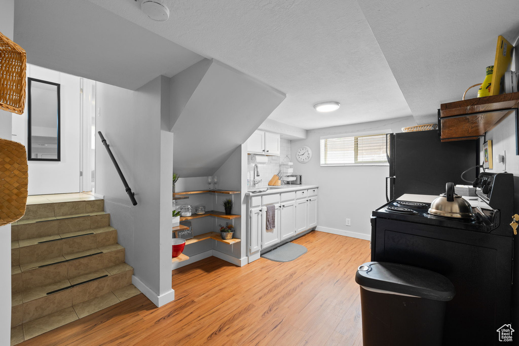 Kitchen with light wood finished floors, white cabinetry, washer / clothes dryer, freestanding refrigerator, and black range with electric cooktop