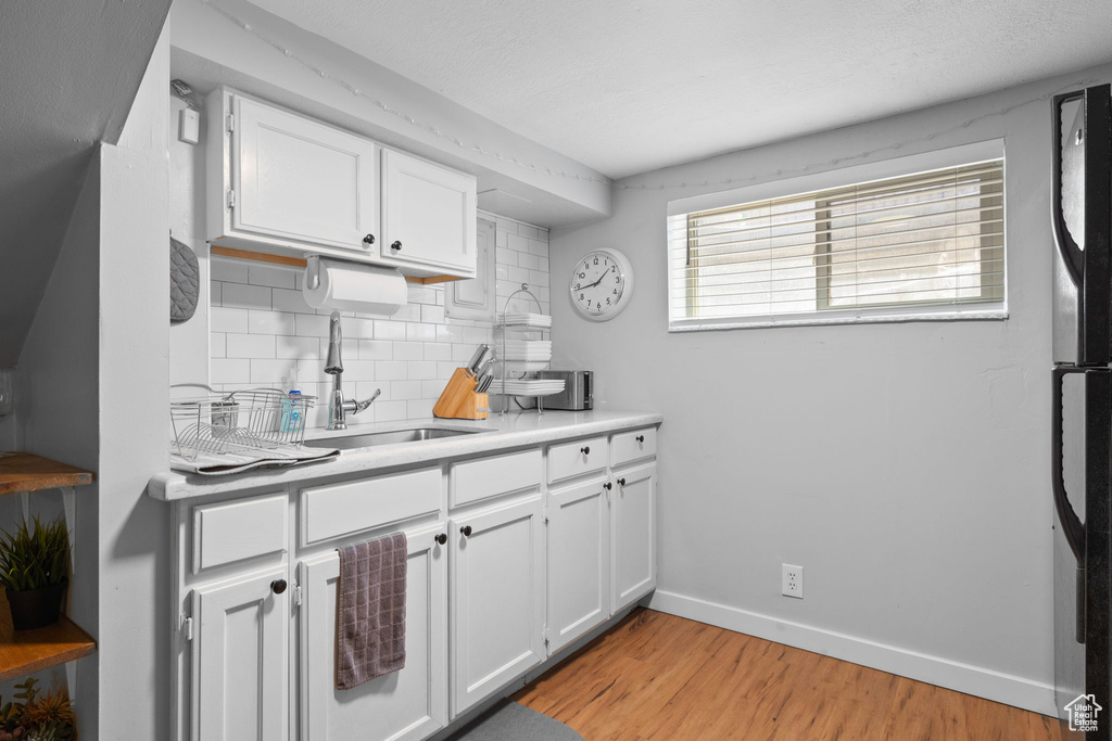 Kitchen featuring decorative backsplash, white cabinetry, light wood finished floors, refrigerator, and light countertops