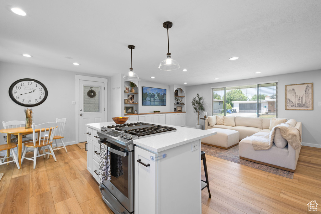 Kitchen with gas range, white cabinets, light wood-style flooring, a kitchen breakfast bar, and recessed lighting