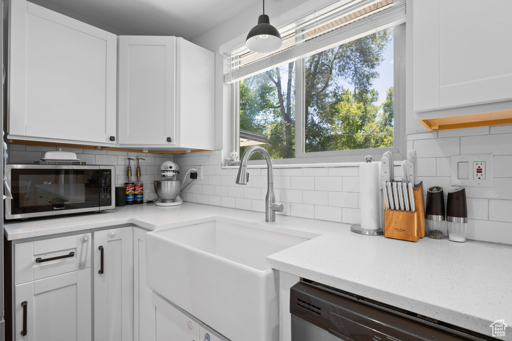 Kitchen featuring stainless steel microwave, dishwashing machine, tasteful backsplash, white cabinets, and light stone counters