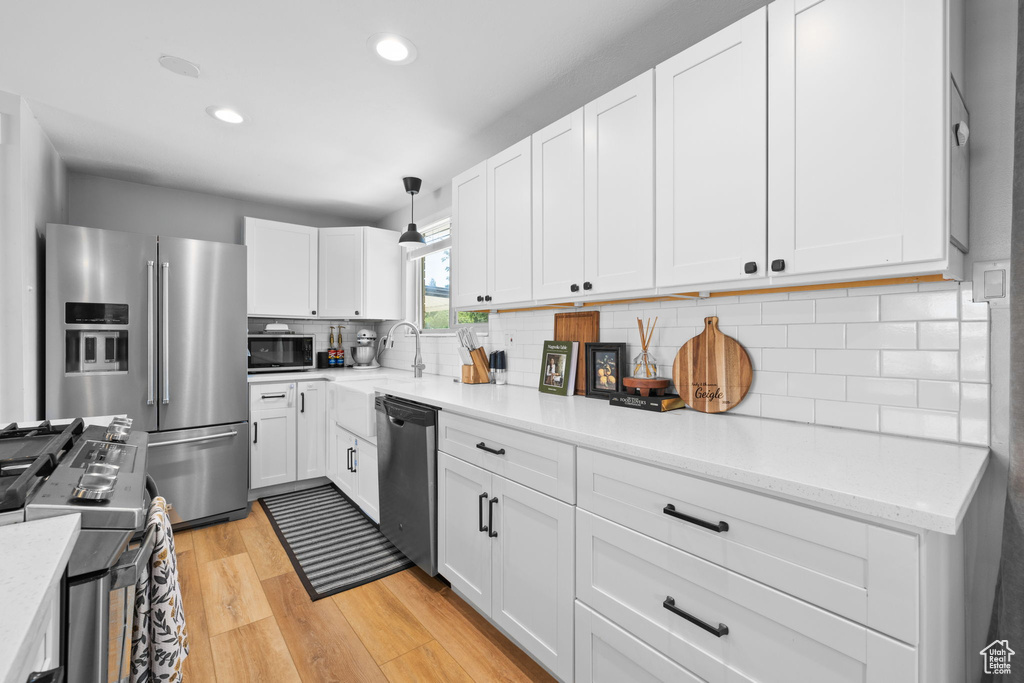 Kitchen with appliances with stainless steel finishes, light wood-style floors, white cabinetry, decorative backsplash, and recessed lighting