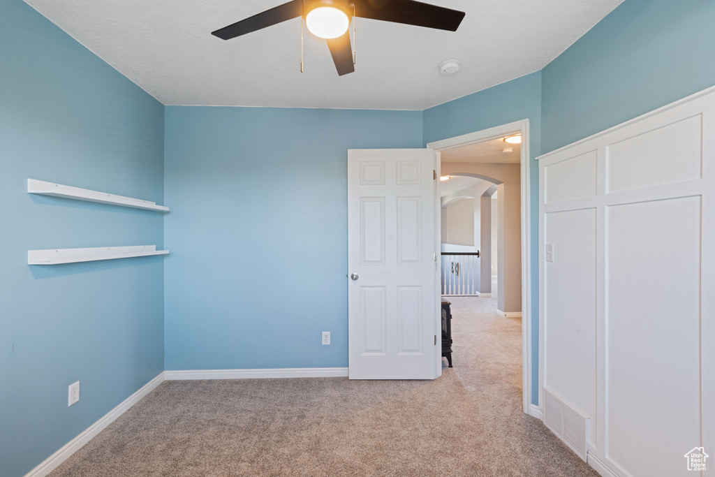 Unfurnished bedroom featuring arched walkways, carpet, a closet, and a ceiling fan