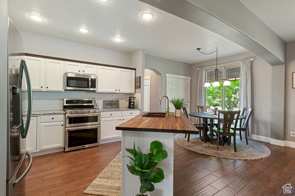 Kitchen with stainless steel appliances, wooden counters, arched walkways, dark wood-type flooring, and backsplash