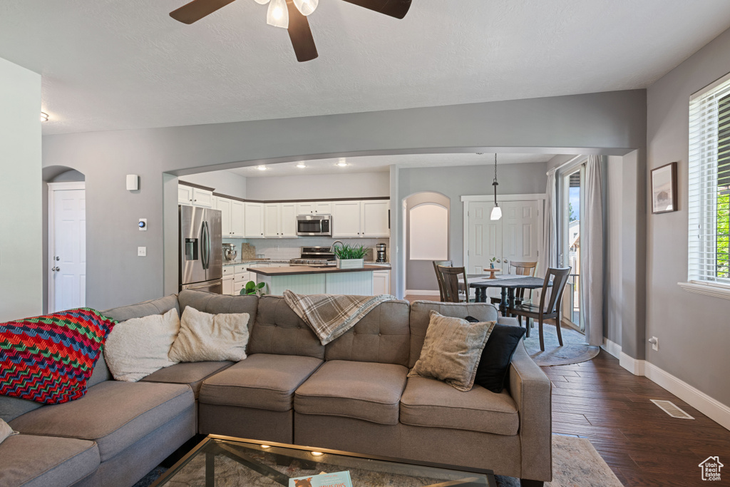 Living area with arched walkways, ceiling fan, and dark wood-type flooring