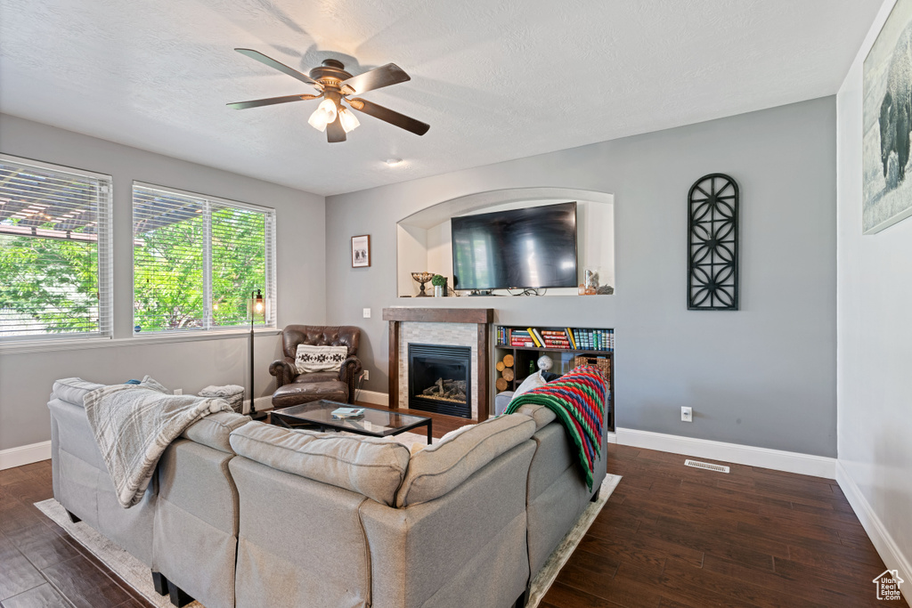 Living room with ceiling fan, dark wood-type flooring, a glass covered fireplace, and a textured ceiling