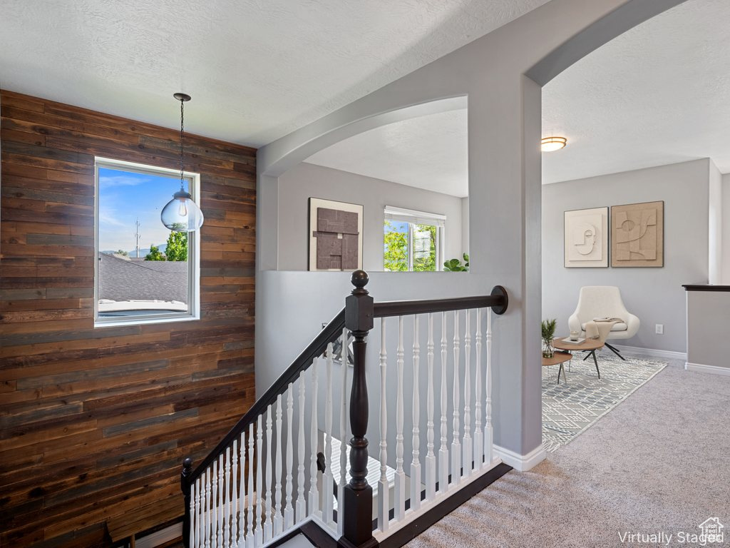 Hall featuring wooden walls, an upstairs landing, carpet, arched walkways, and a textured ceiling