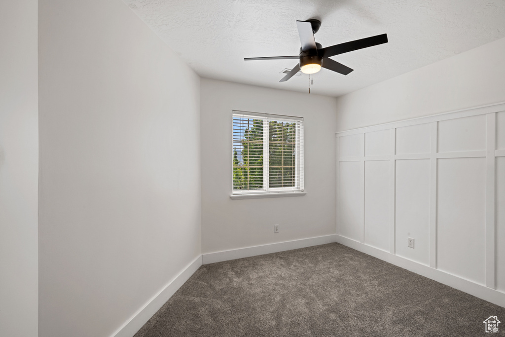 Spare room featuring dark colored carpet, a ceiling fan, and a textured ceiling