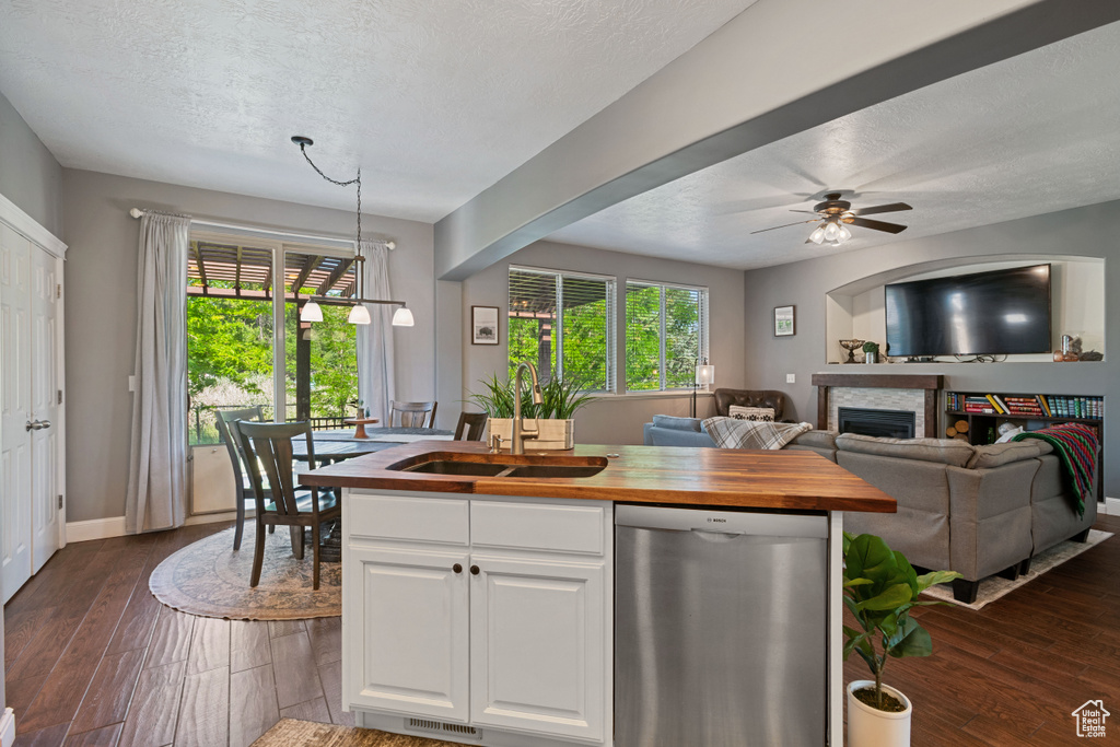 Kitchen with stainless steel dishwasher, butcher block countertops, a textured ceiling, white cabinets, and dark wood-style flooring
