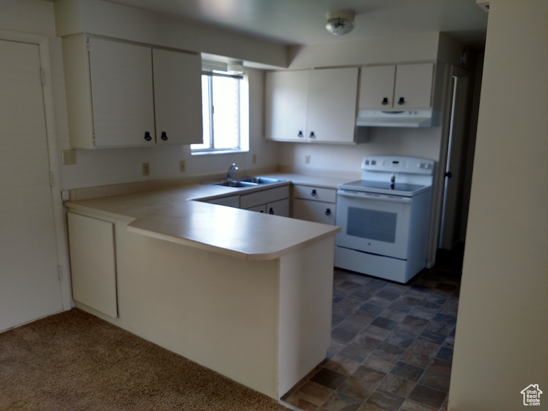 Kitchen with white electric stove, ventilation hood, a peninsula, white cabinetry, and light countertops