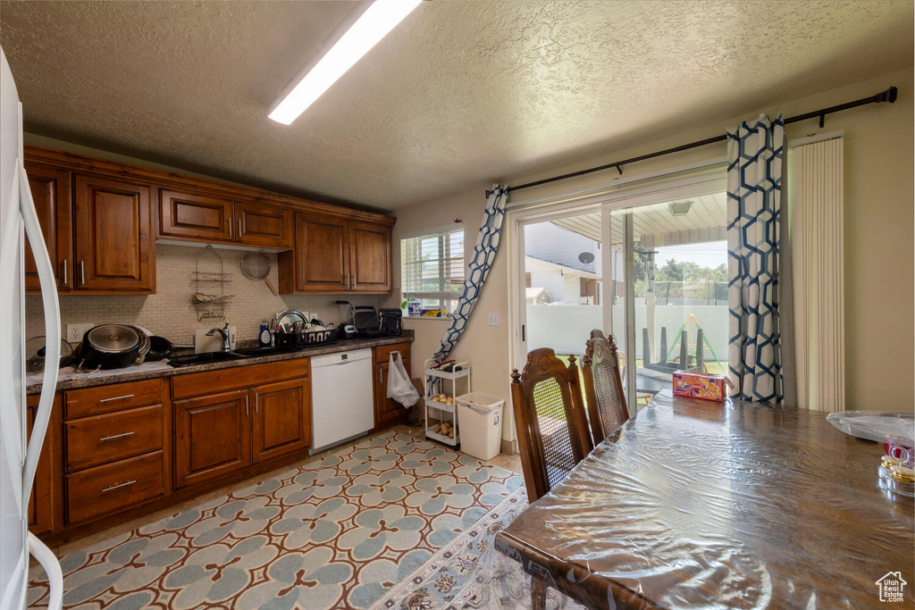 Kitchen with white appliances, a textured ceiling, dark countertops, brown cabinets, and decorative backsplash