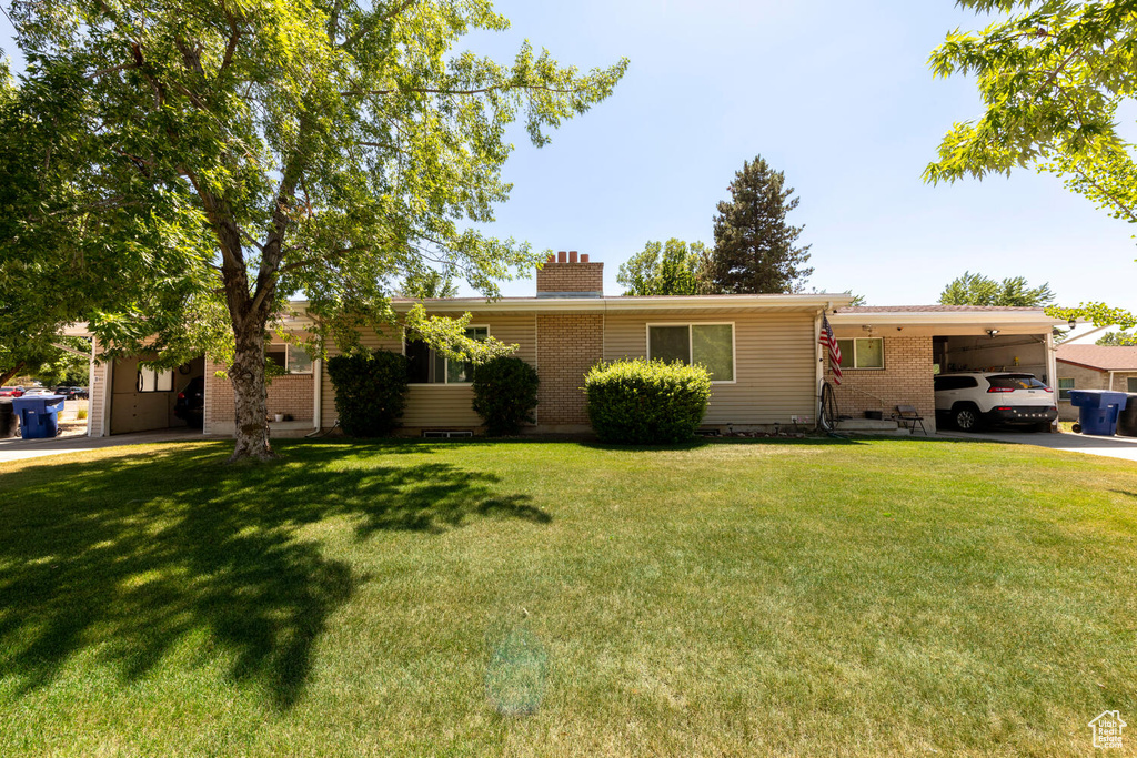 Single story home featuring a chimney, a carport, brick siding, and a front yard