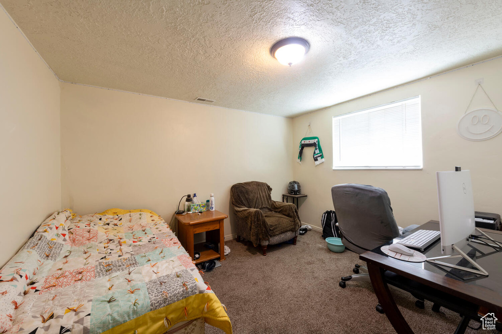 Bedroom with a textured ceiling, carpet floors, and an office area