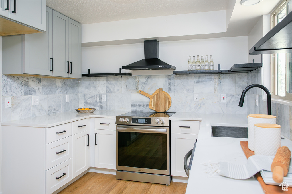 Kitchen featuring open shelves, electric stove, wall chimney exhaust hood, and light countertops