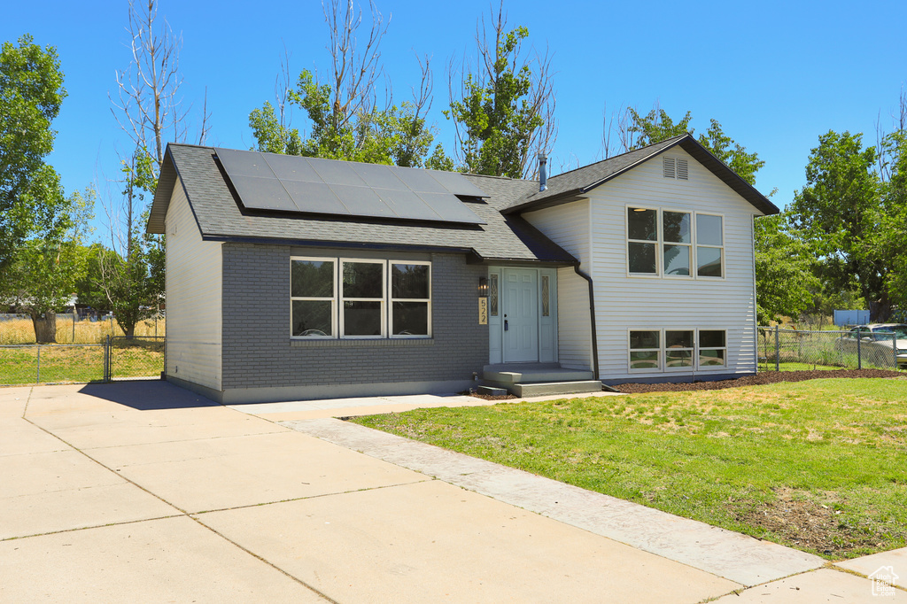 Split level home featuring solar panels, a shingled roof, and brick siding