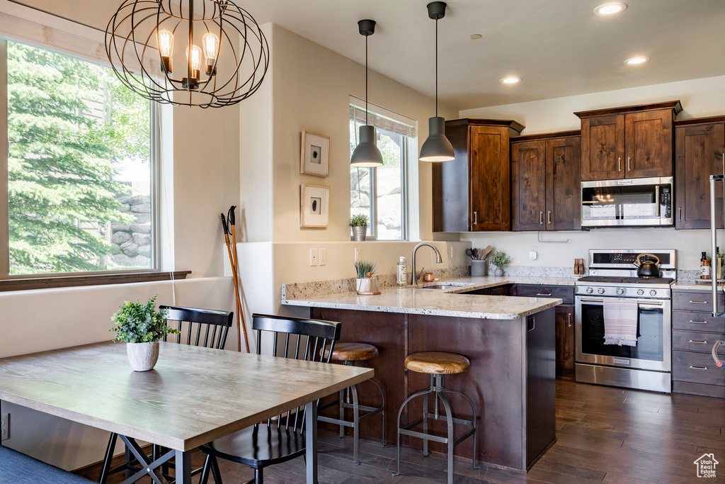 Kitchen with stainless steel appliances, light stone countertops, recessed lighting, a peninsula, and hanging light fixtures