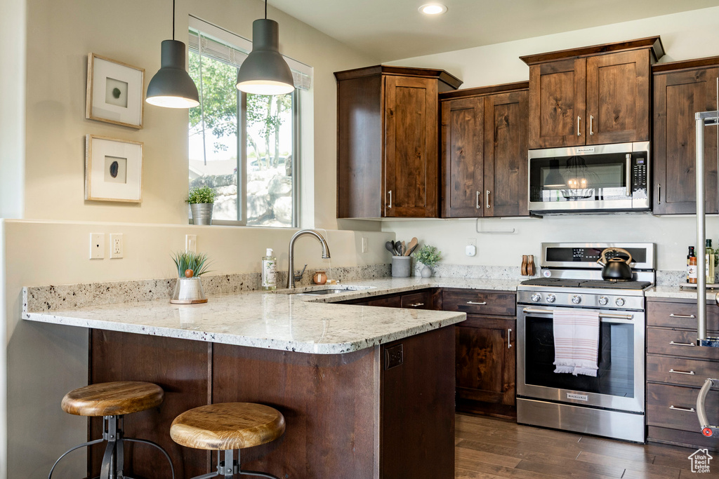 Kitchen featuring appliances with stainless steel finishes, light stone countertops, a peninsula, dark wood-style flooring, and a breakfast bar