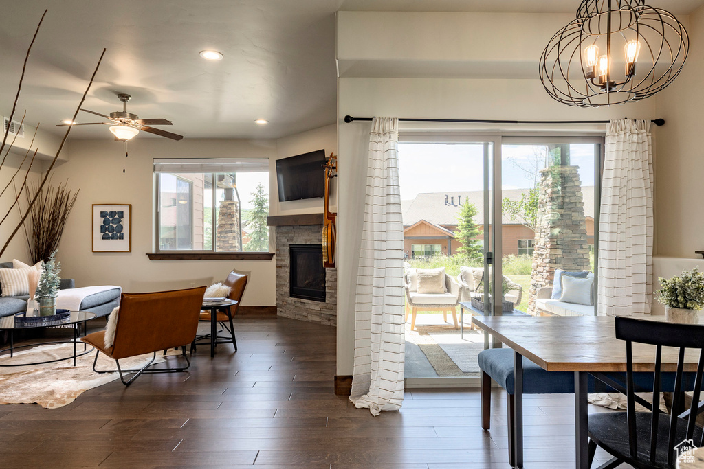 Dining space with a stone fireplace, dark wood finished floors, a ceiling fan, recessed lighting, and a chandelier