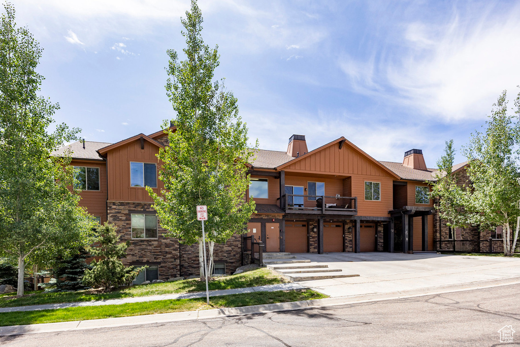 Townhome / multi-family property featuring stone siding, an attached garage, board and batten siding, and concrete driveway