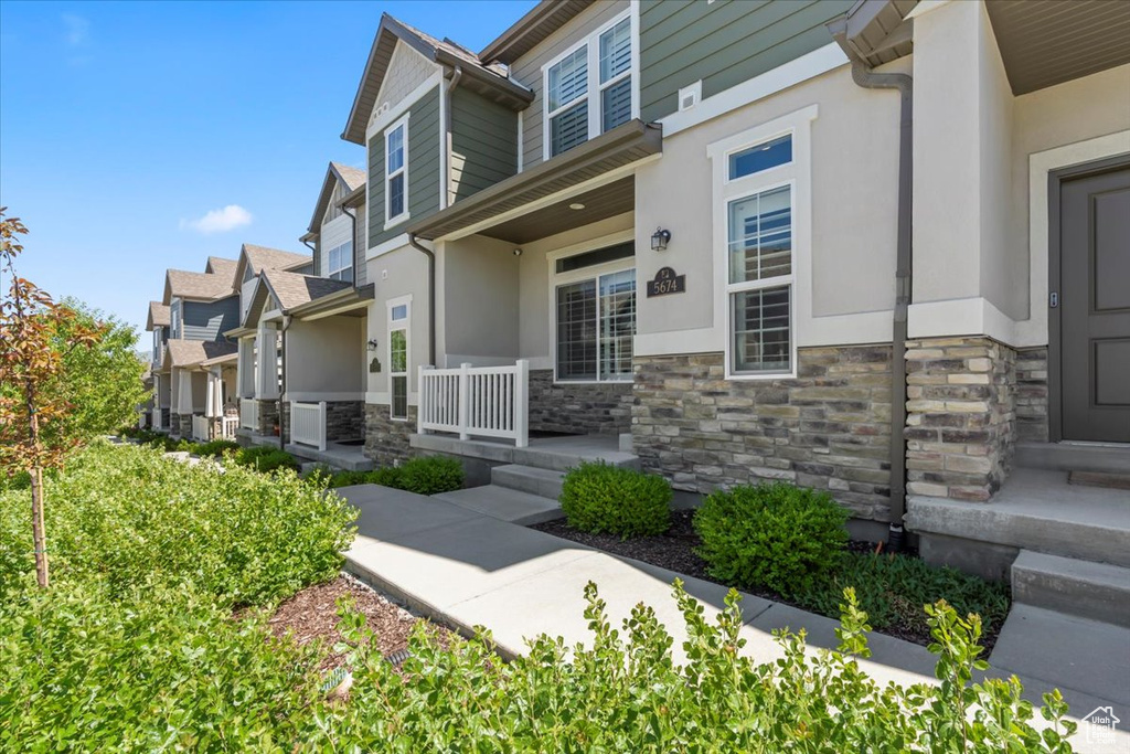 View of exterior entry featuring stone siding, covered porch, stucco siding, and a residential view