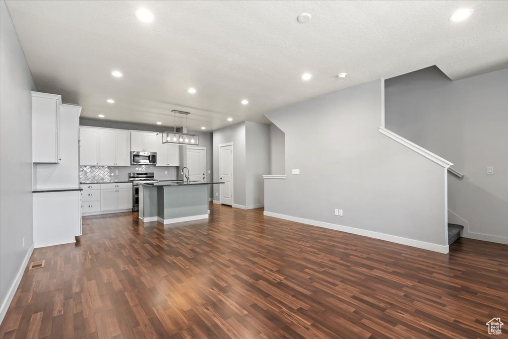 Unfurnished living room featuring dark wood-type flooring, recessed lighting, and stairs