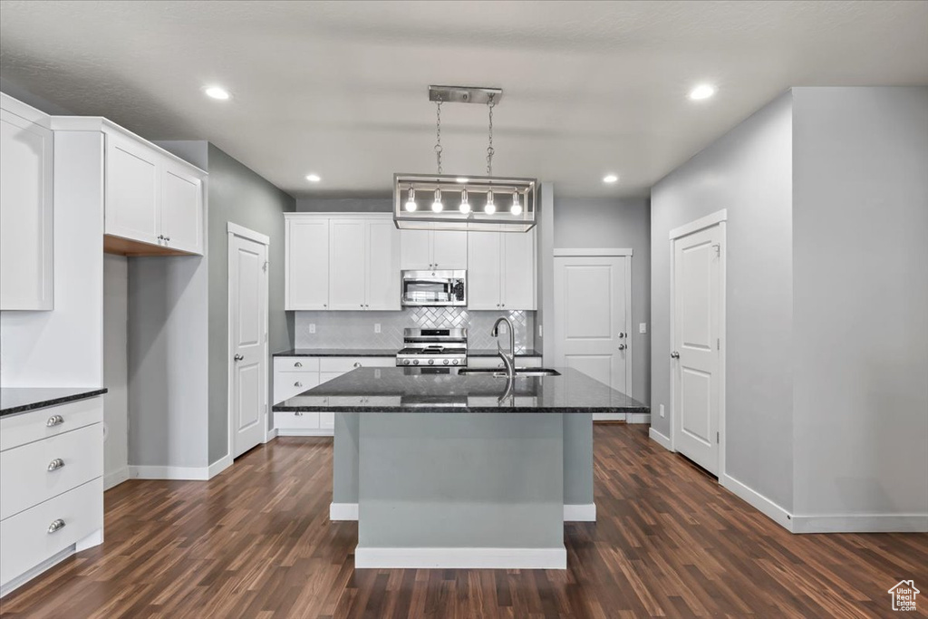 Kitchen with stainless steel appliances, dark wood finished floors, tasteful backsplash, white cabinets, and an island with sink