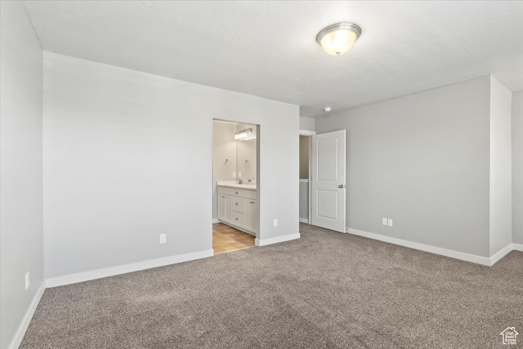 Unfurnished bedroom with light carpet, ensuite bathroom, and a textured ceiling