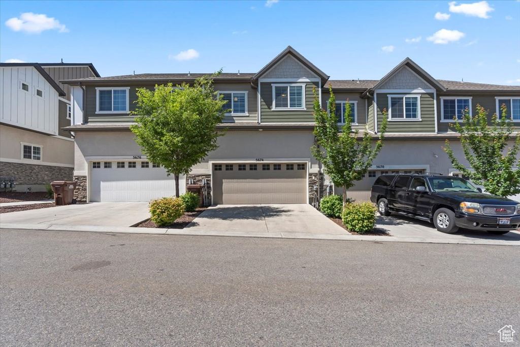 Multi unit property featuring stone siding, a garage, driveway, and stucco siding