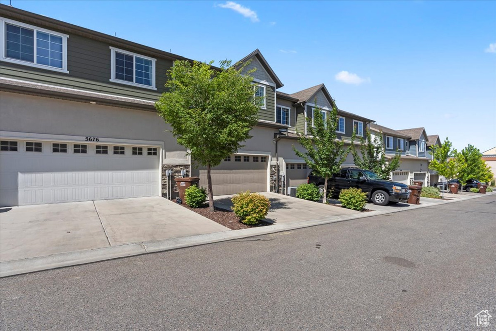 View of property featuring stone siding, a garage, a residential view, driveway, and stucco siding