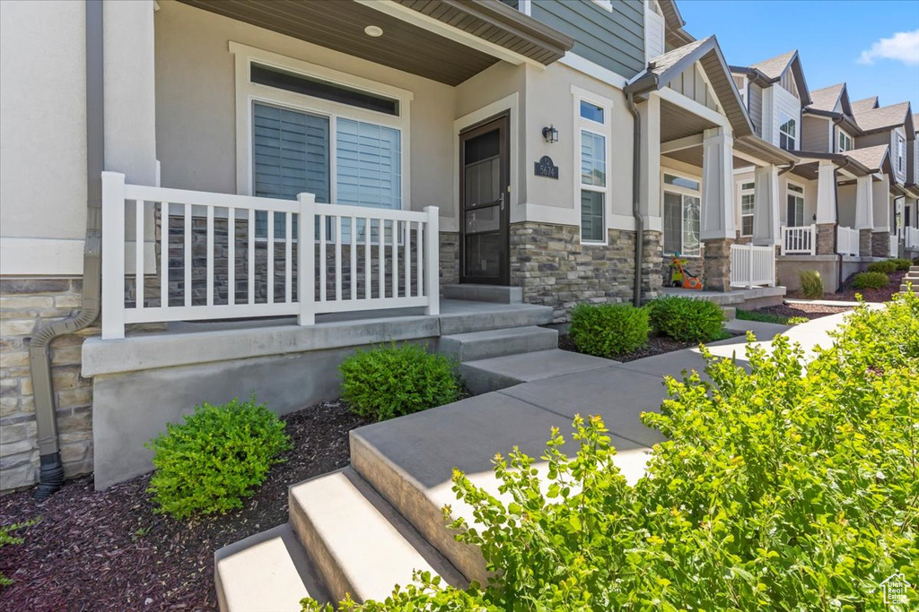 Property entrance with a porch, stone siding, a residential view, and stucco siding