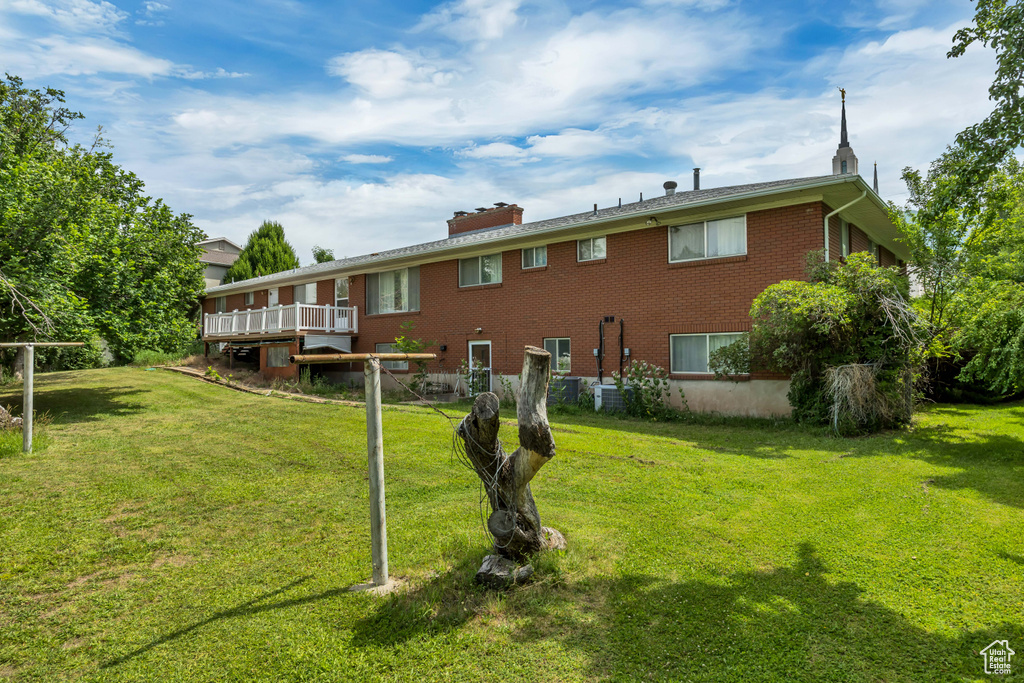 Back of property with brick siding, a lawn, a wooden deck, and a chimney
