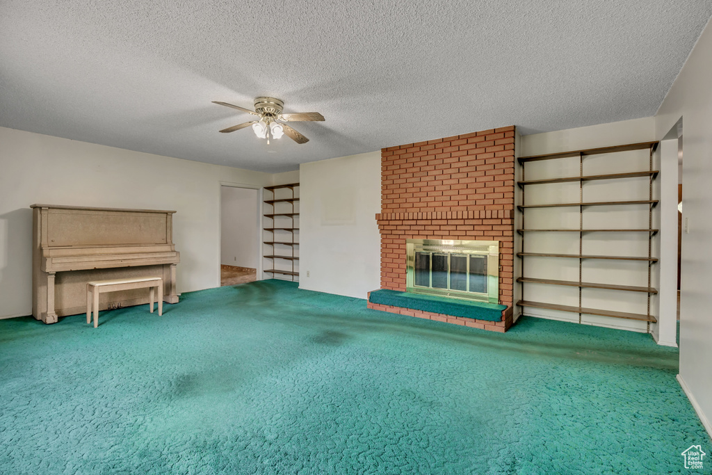 Unfurnished living room with a ceiling fan, a brick fireplace, carpet, and a textured ceiling