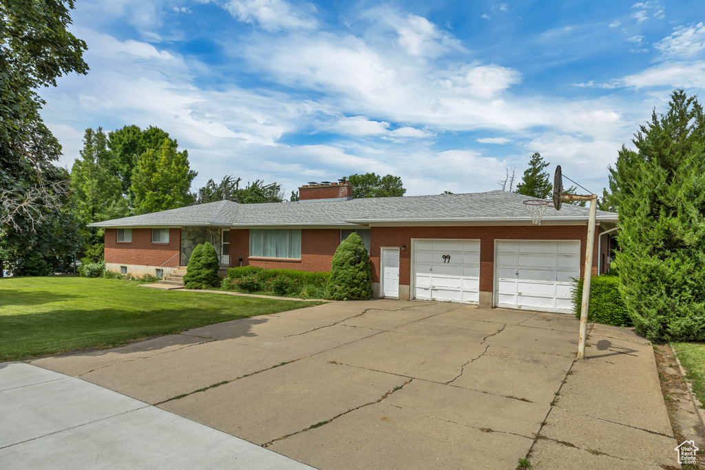 Single story home with a garage, brick siding, a front lawn, driveway, and a chimney