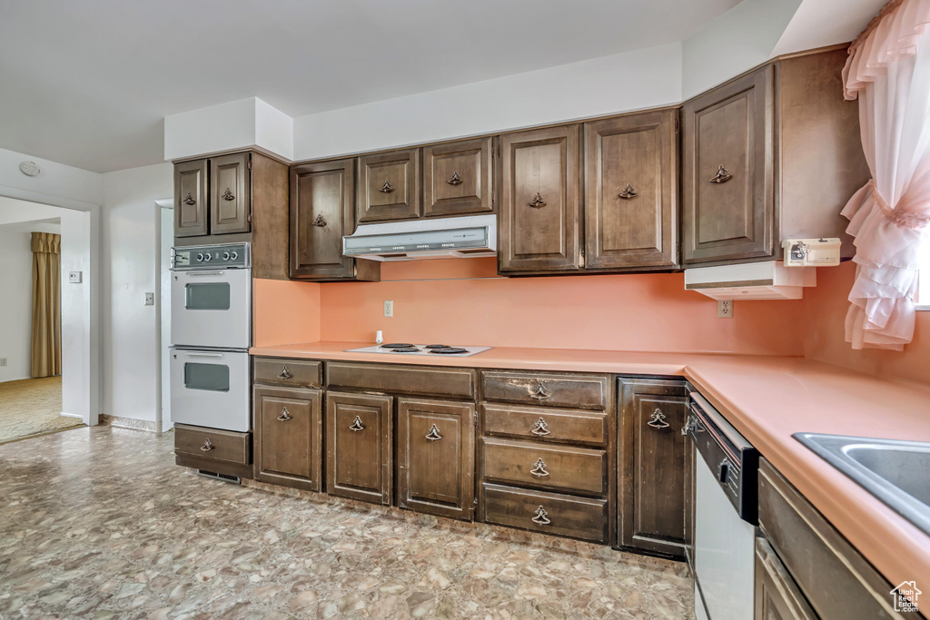 Kitchen with white appliances, under cabinet range hood, light countertops, and dark brown cabinetry