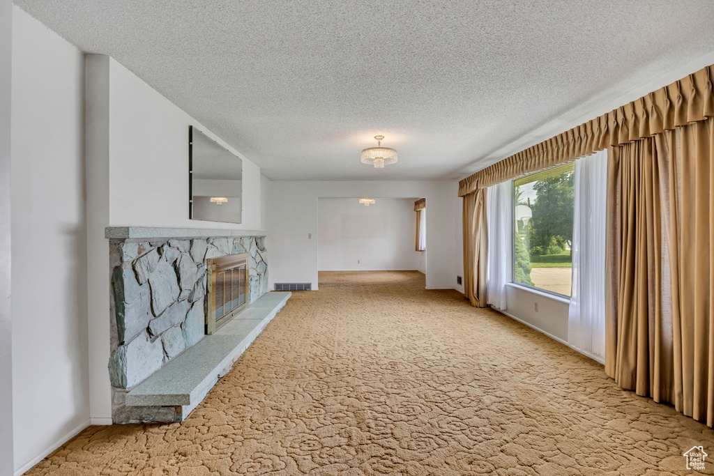 Unfurnished living room with carpet, a textured ceiling, and a stone fireplace