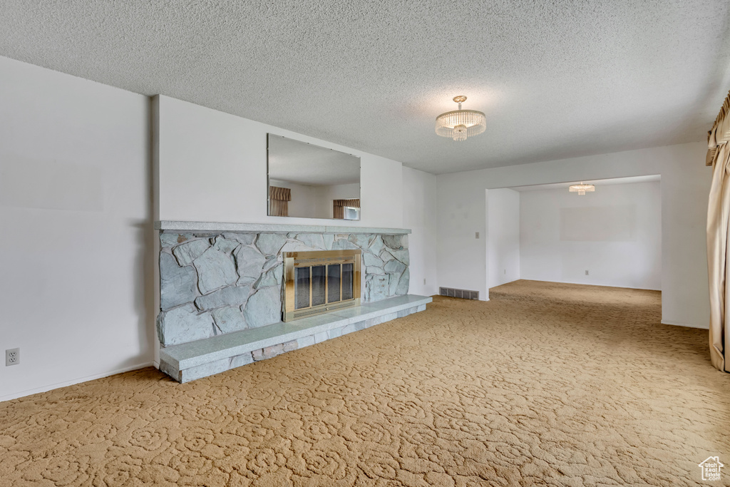 Unfurnished living room featuring carpet floors, a stone fireplace, and a textured ceiling