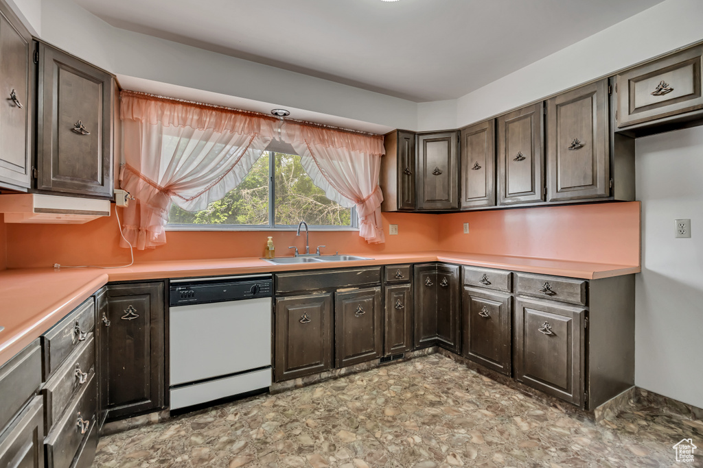 Kitchen with white dishwasher, light countertops, dark brown cabinetry, and stone finish floors