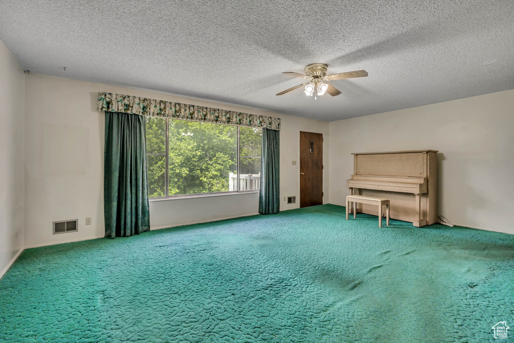 Unfurnished living room with ceiling fan, carpet flooring, and a textured ceiling
