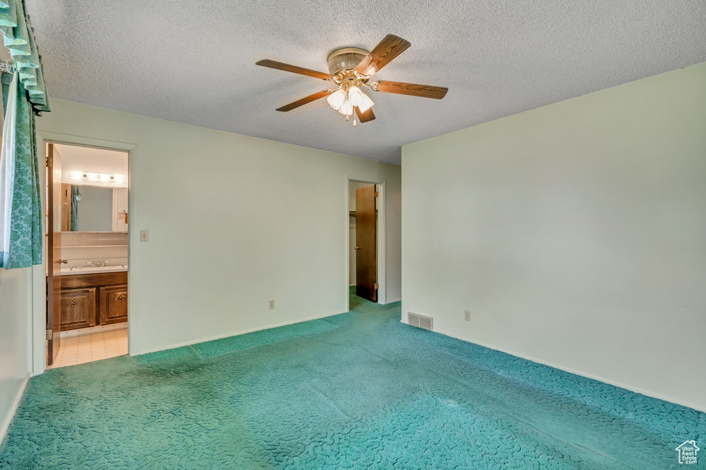 Unfurnished bedroom featuring carpet floors, a textured ceiling, connected bathroom, and a ceiling fan