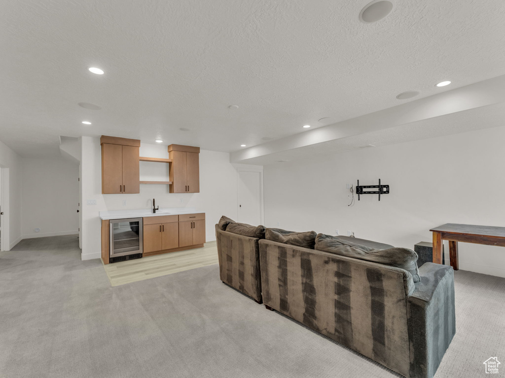 Living room with beverage cooler, bar with sink, light carpet, recessed lighting, and a textured ceiling